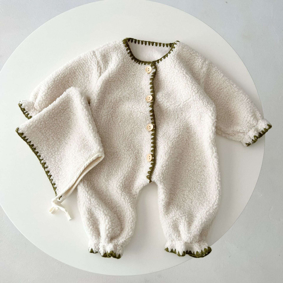 Ivory sherpa romper with stitched cuffs and ankles, flat lay