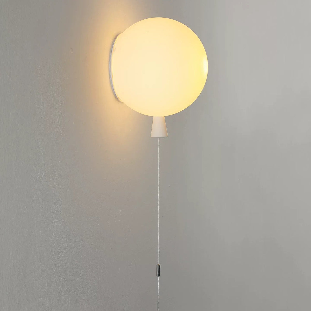 White balloon wall lamp glowing warm on a grey wall