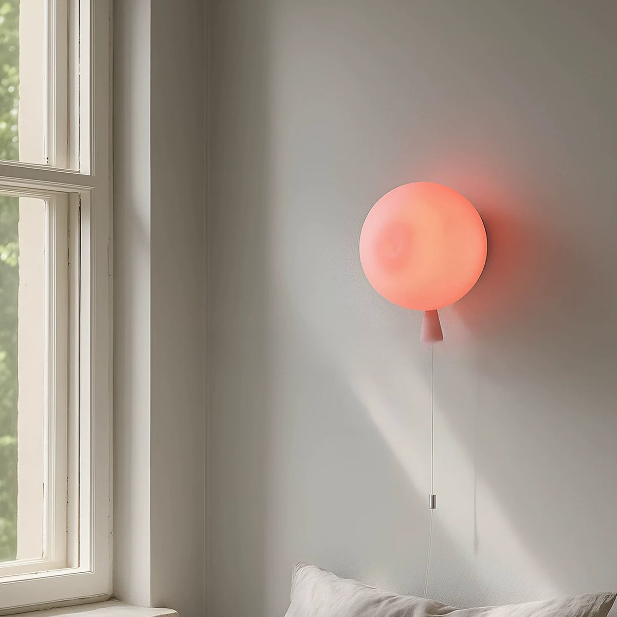 Pink balloon wall lamp glowing beside a window above a bed