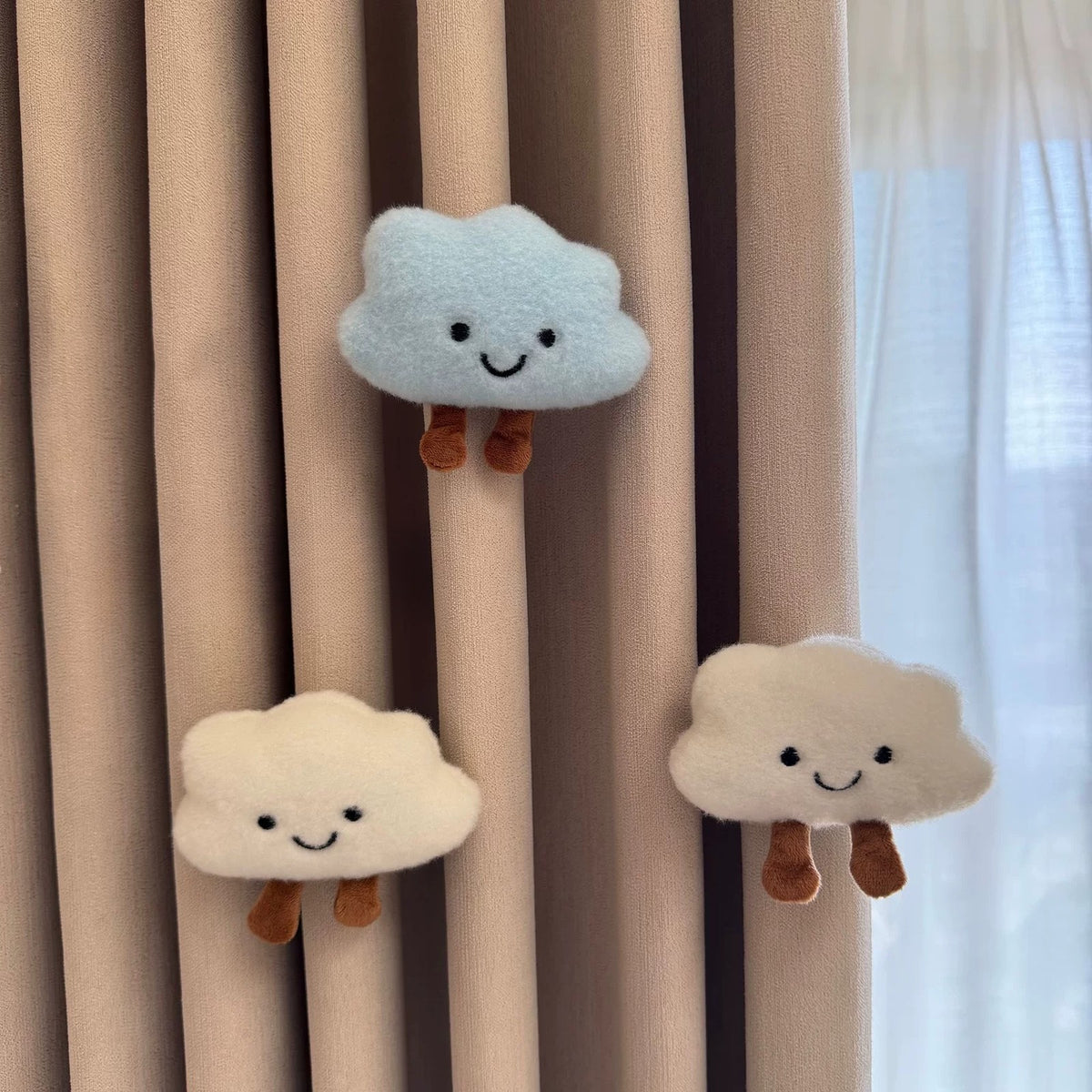Three smiling plush clouds pinned to curtains by a sunny window