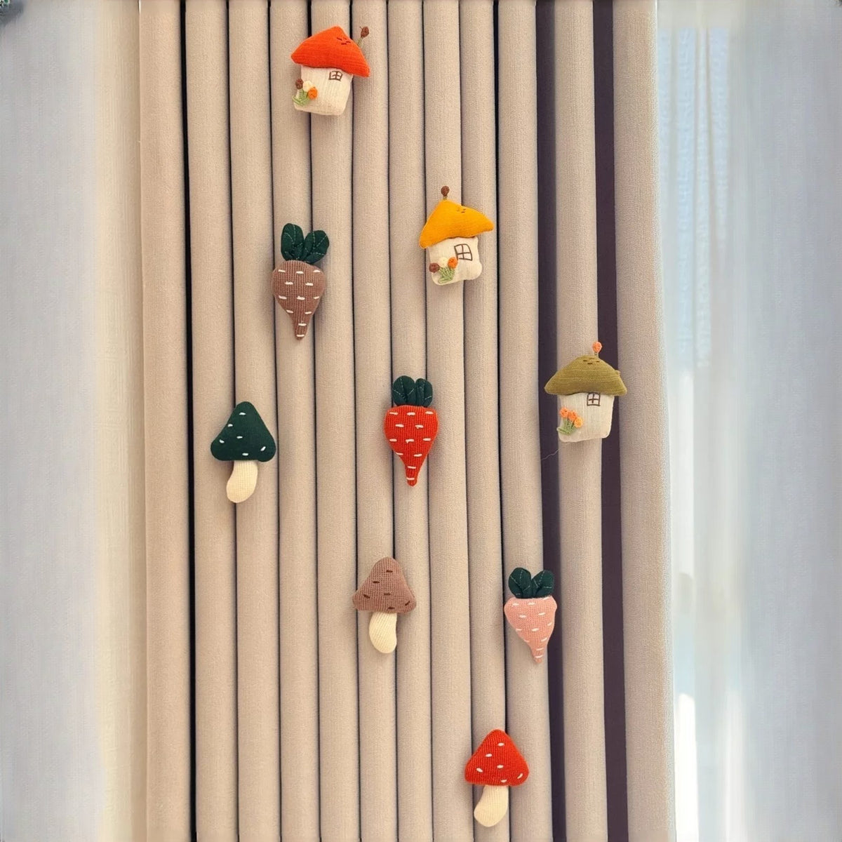 Knitted mushroom, carrot and little house charms pinned on beige curtains