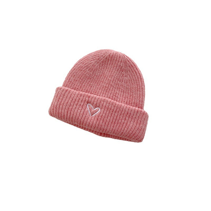 Soft pink knitted beanie with a ribbed texture and a small embroidered heart detail on the cuff. This cozy and stylish winter hat adds a charming touch to any cold-weather outfit, perfect for those looking for a playful yet subtle accessory. The minimalist design makes it suitable for both kids and adults. Ideal for display in e-commerce listings or winter fashion catalogs.