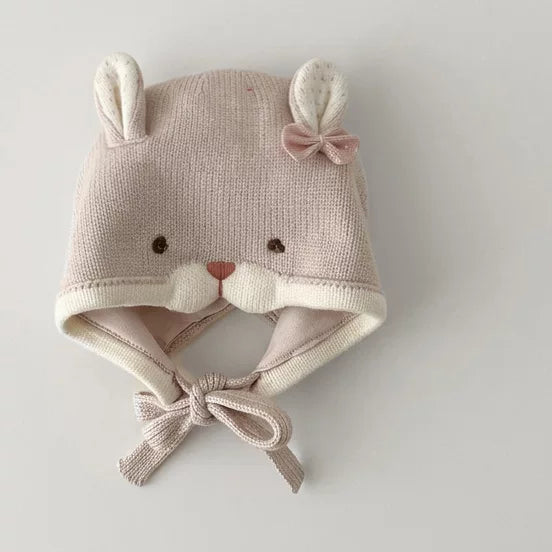 Soft pink knit bunny baby bonnet with bow and chin ties, flat lay