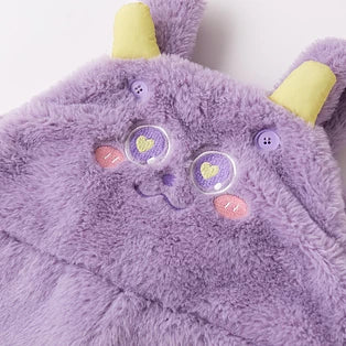 Detail of the lilac plush overalls bib with embroidered eyes and yellow horns