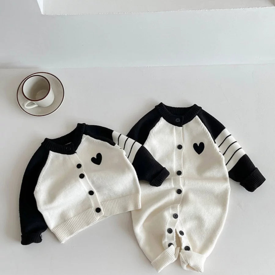 Cream and black heart knit baby romper with the matching cardigan, flat lay
