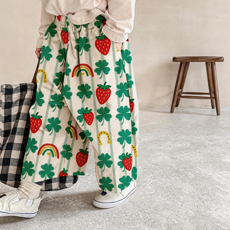 Child wearing cream wide-leg pants with green clover, rainbow and strawberry print
