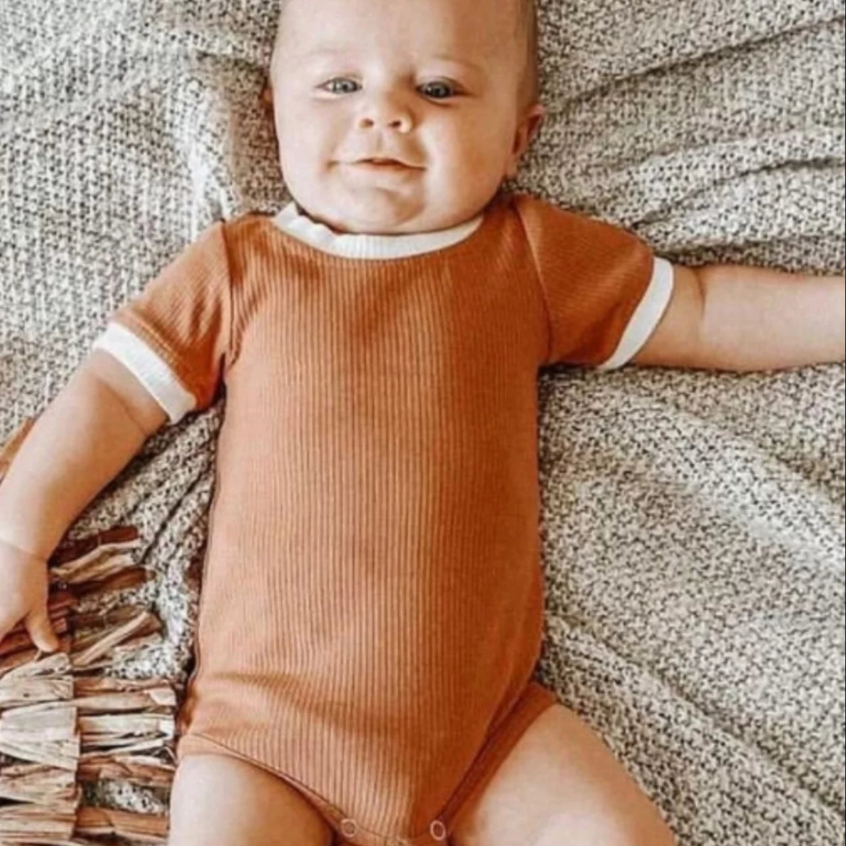 Smiling baby lying on a knit blanket in a caramel ribbed short sleeve bodysuit