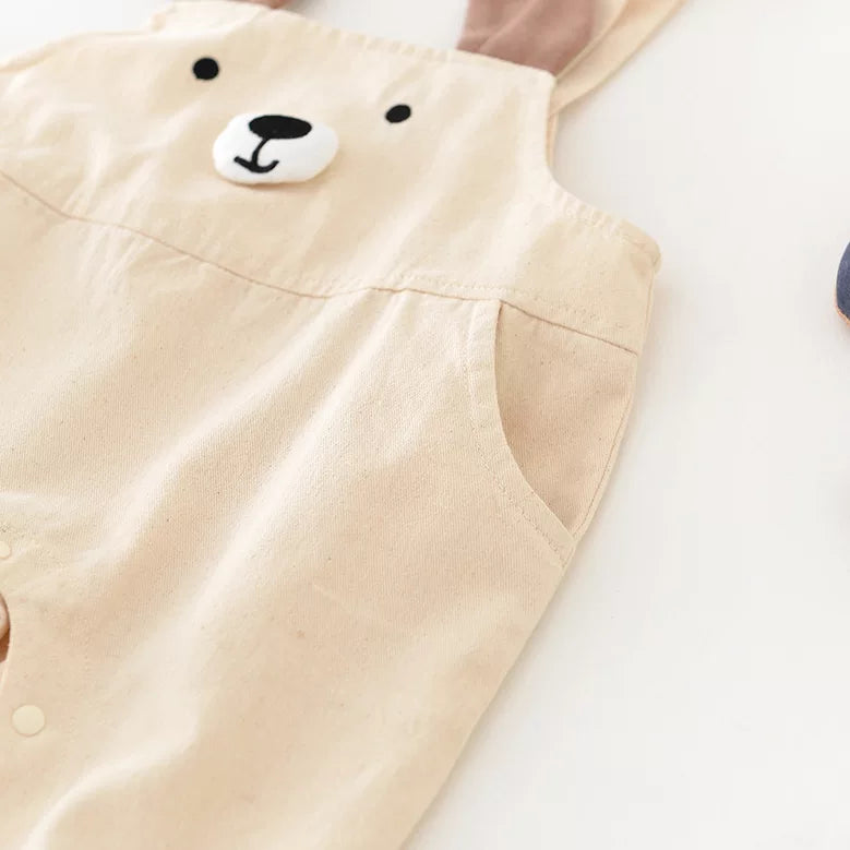 Close-up of the stitched bear face and side pocket on beige cotton overalls