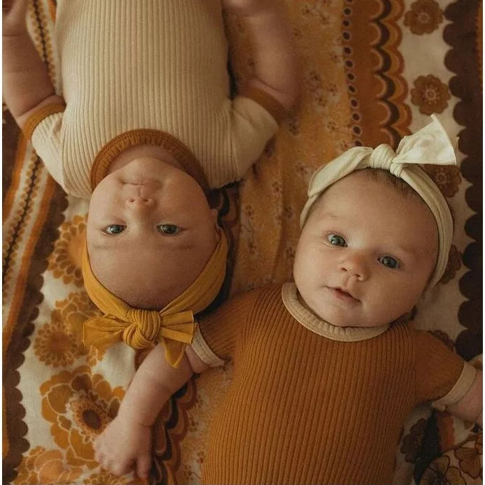 Two babies in apricot and caramel ribbed bodysuits lying side by side