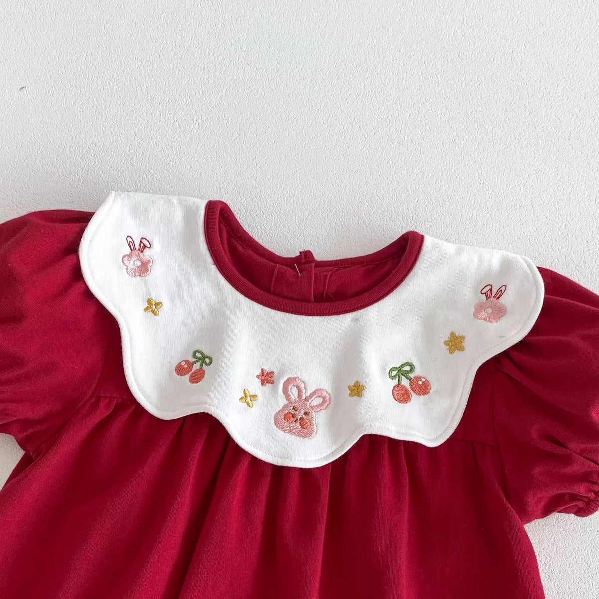 Close-up of the white scalloped collar embroidered with bunnies, cherries and stars