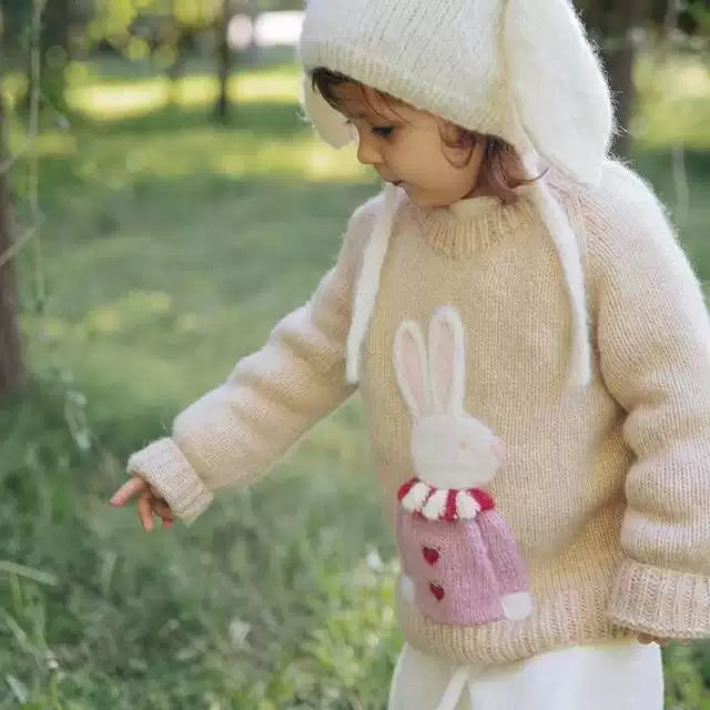 Girl exploring the grass in a cream bunny knit jumper