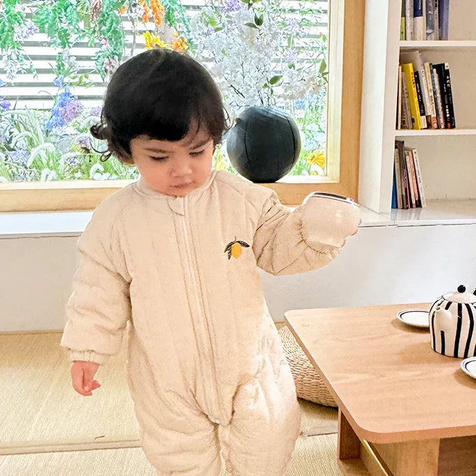 Toddler walking indoors in a cream quilted lemon romper