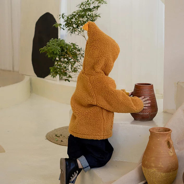 Toddler in a mustard sherpa jacket playing with a clay pot