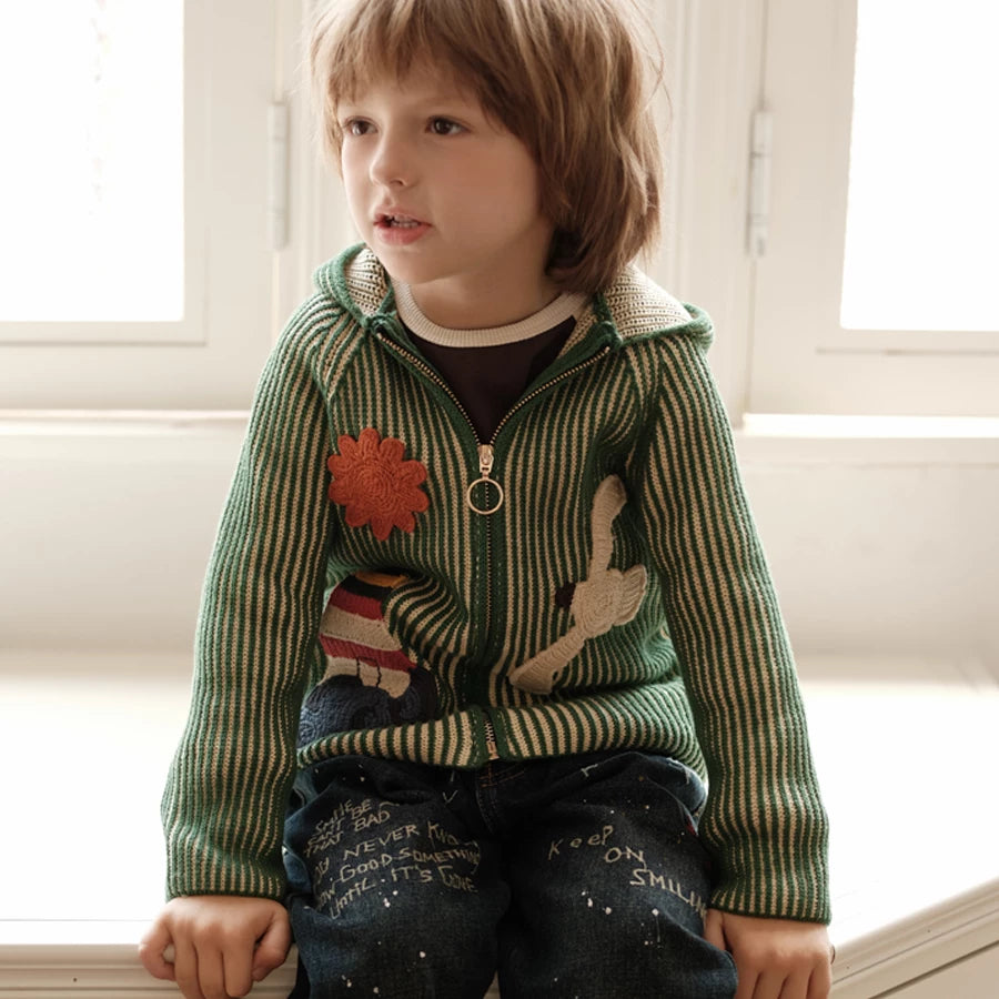 Boy sitting on a windowsill in a green hooded knit cardigan