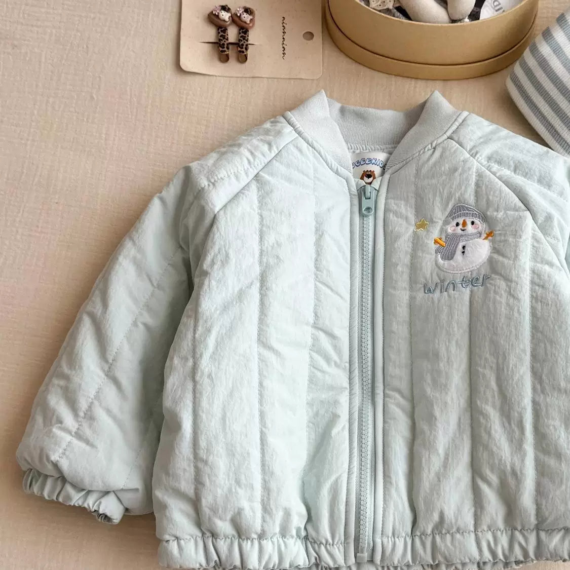 Mint quilted girls jacket with front zip and snowman embroidery, flat lay
