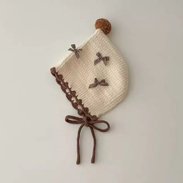 Cream knit pixie bonnet with brown scalloped trim and ties, flat lay