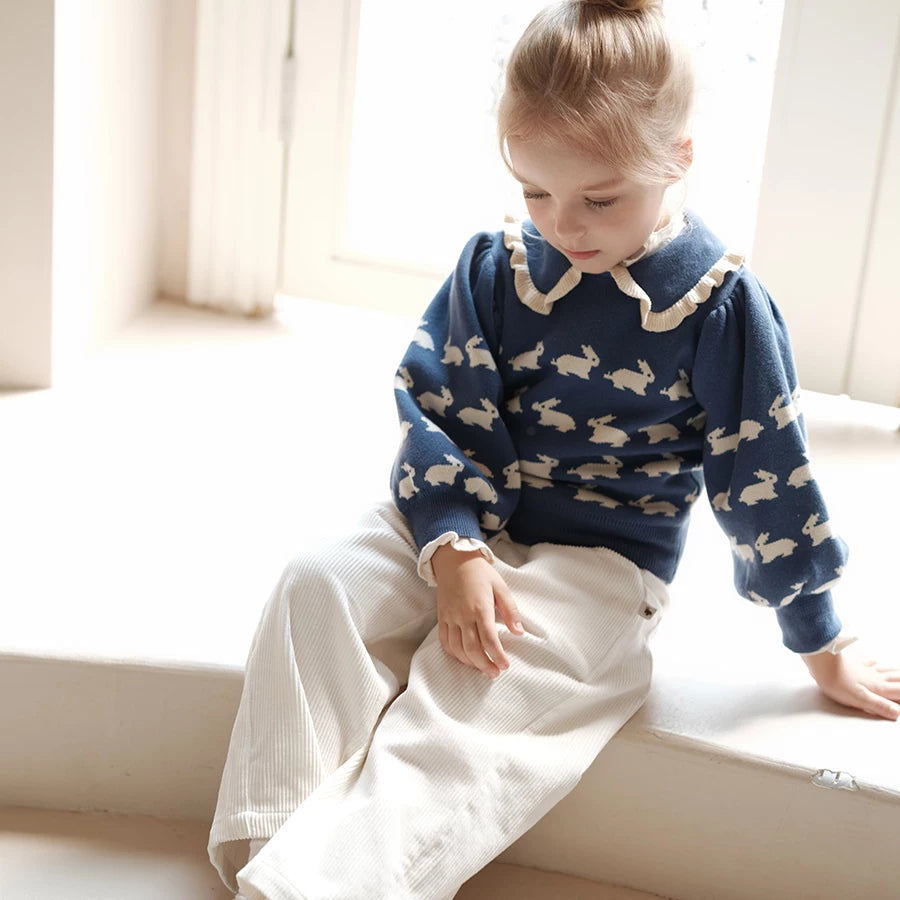Girl sitting by a window in a bunny print knit jumper