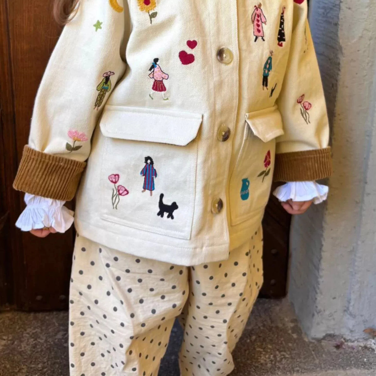 Toddler in a cream embroidered jacket with polka dot trousers and ruffled cuffs