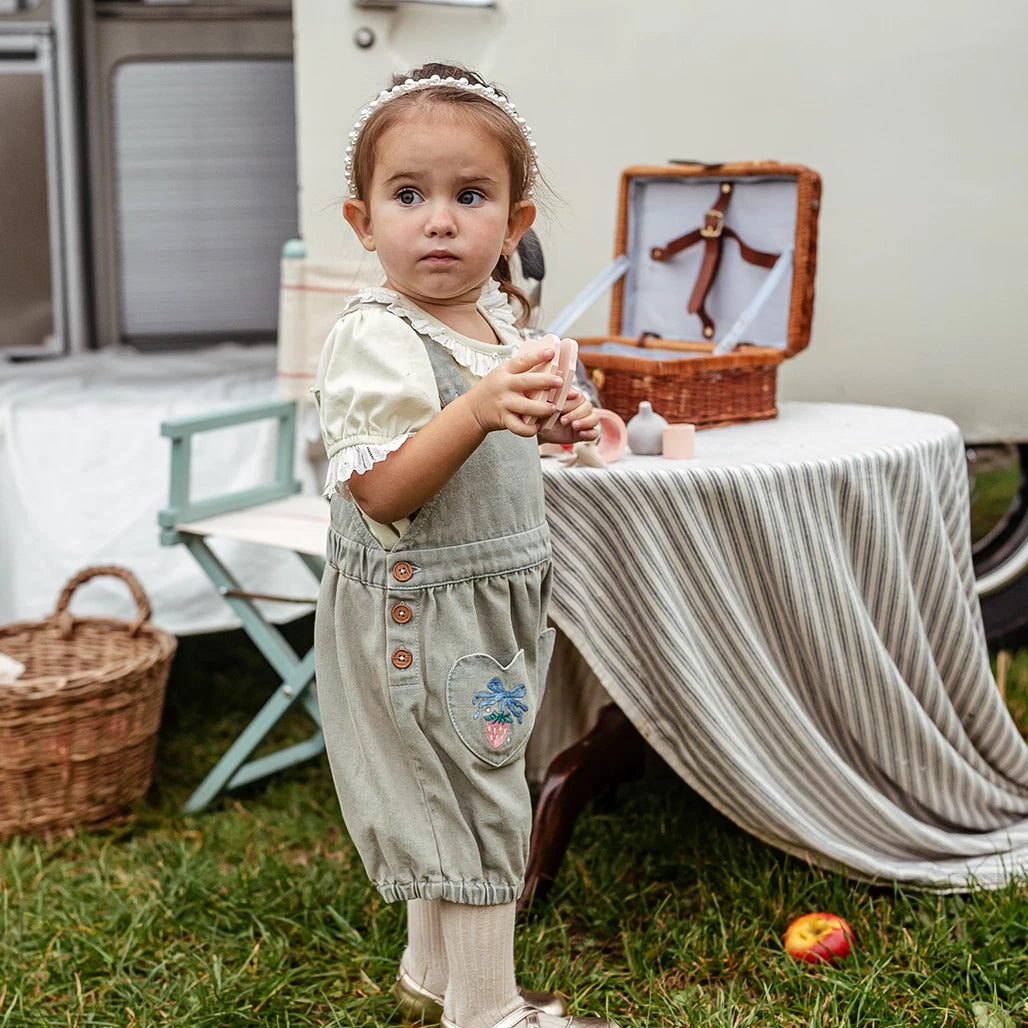 Toddler in sage green bubble shortalls beside a picnic table
