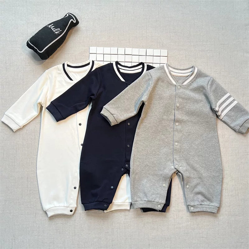 Snow white, navy and heather grey varsity baby rompers laid flat side by side