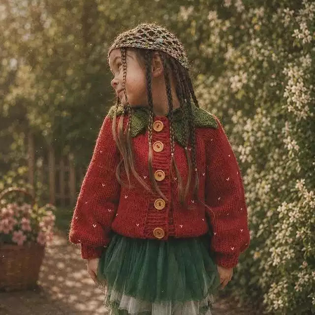Girl in a strawberry knit cardigan with green leaf collar in a garden