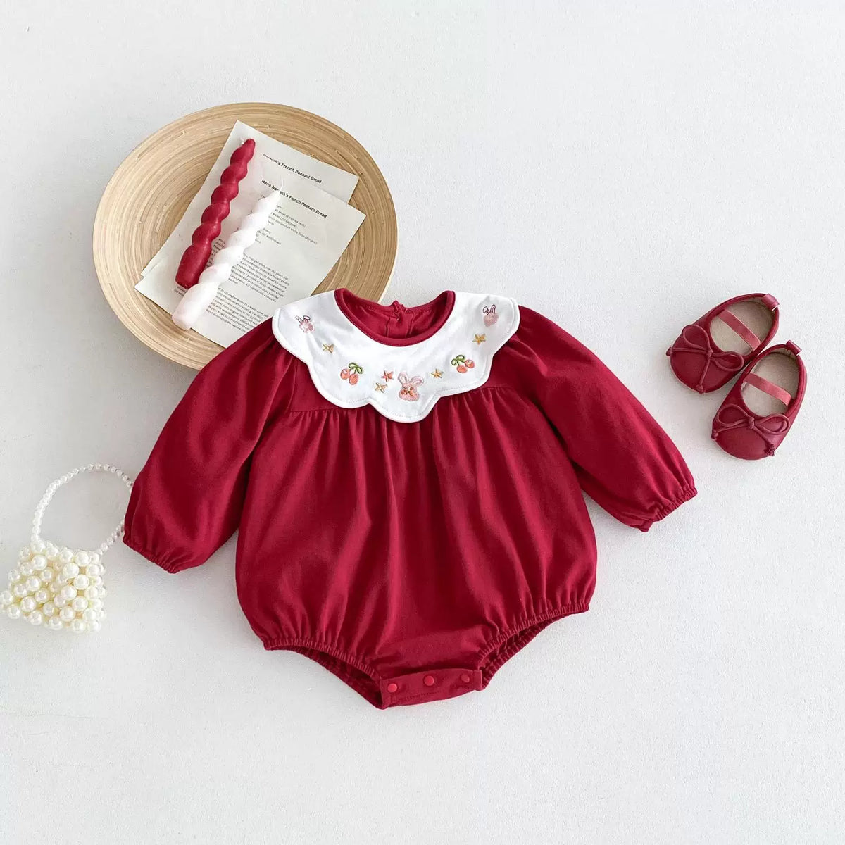 Red long-sleeve baby bodysuit with bunny and cherry embroidered collar, flat lay