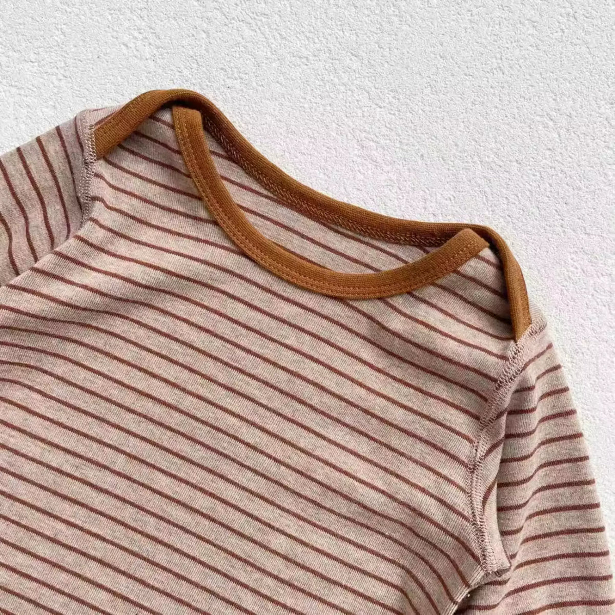 Close-up of caramel neck trim on a mocha striped baby romper
