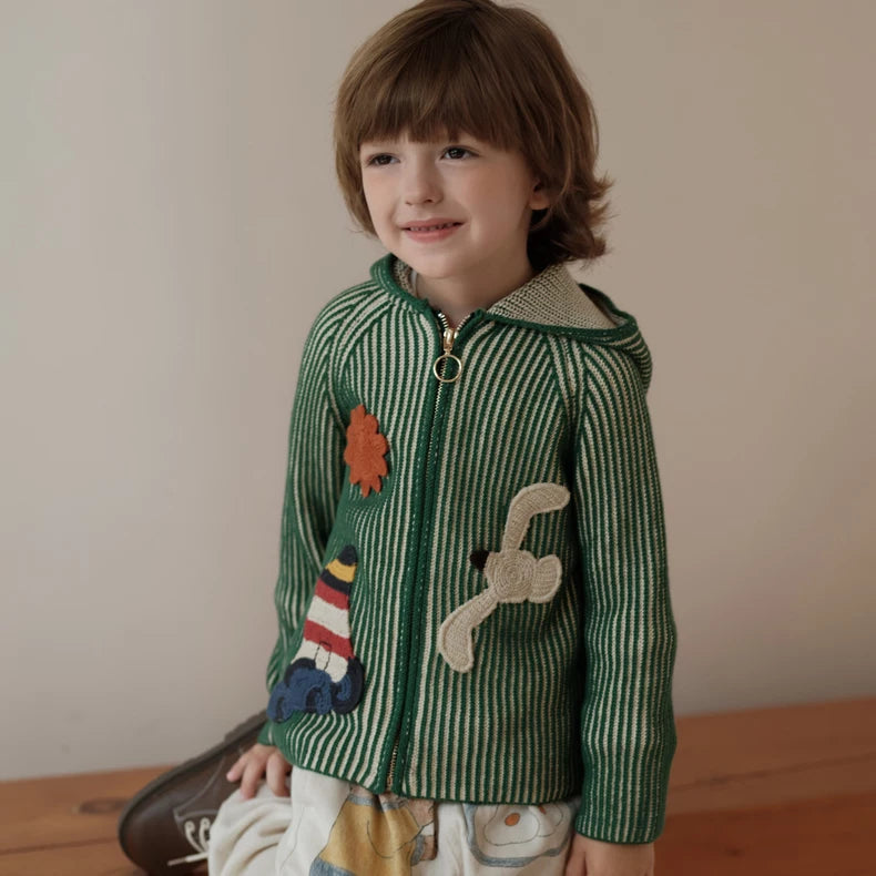 Smiling child in a green knit cardigan with lighthouse appliqué