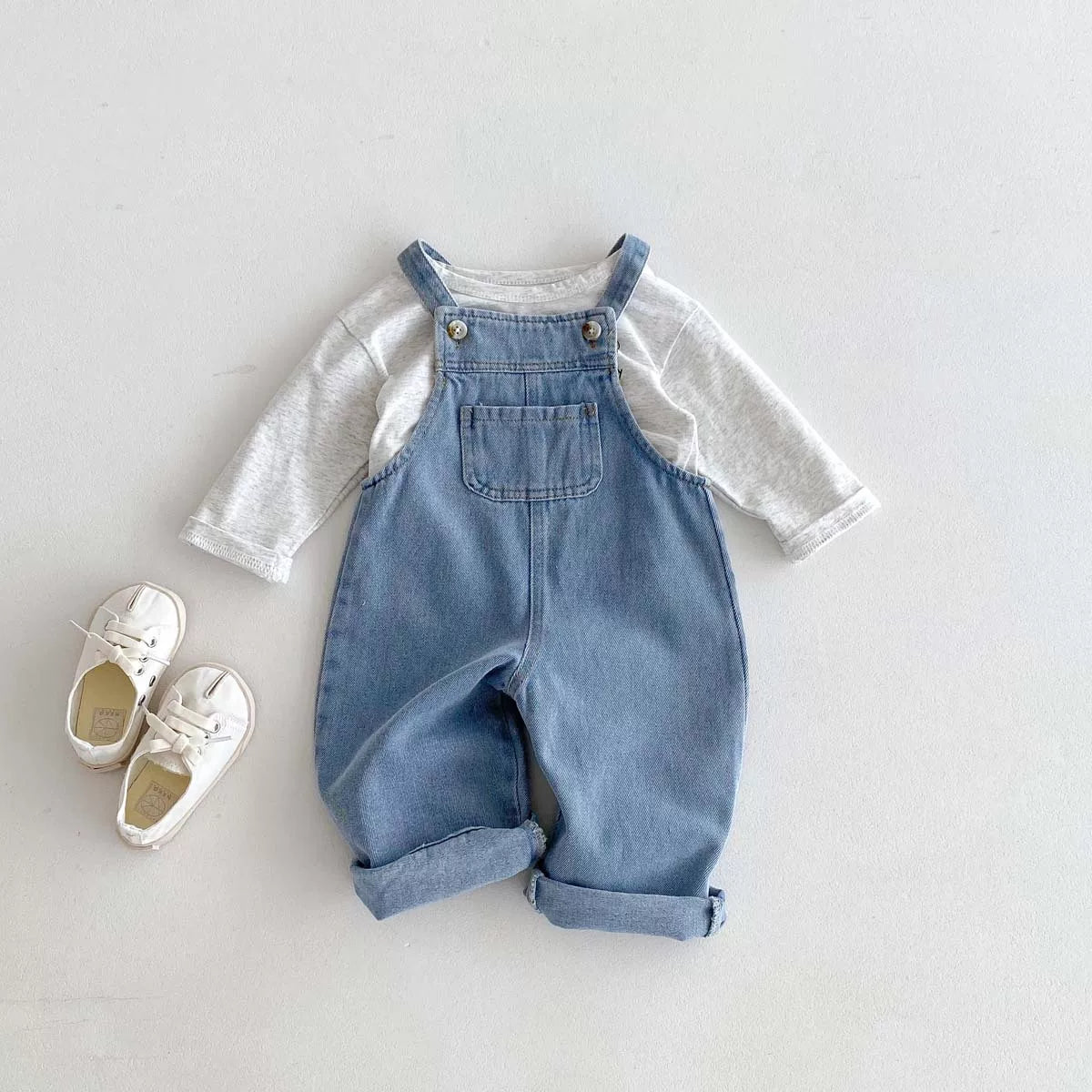 Denim overalls styled with a white long-sleeve tee and sneakers