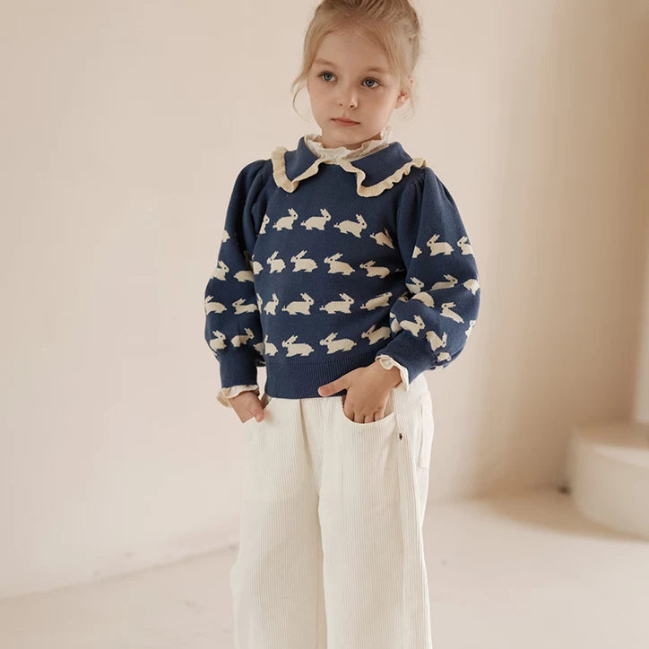 Girl wearing a navy bunny knit sweater with ruffle collar and cream trousers