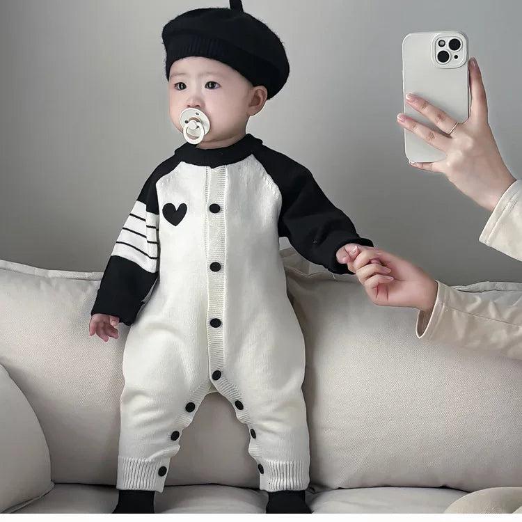 Baby standing in the heart knit romper holding a hand