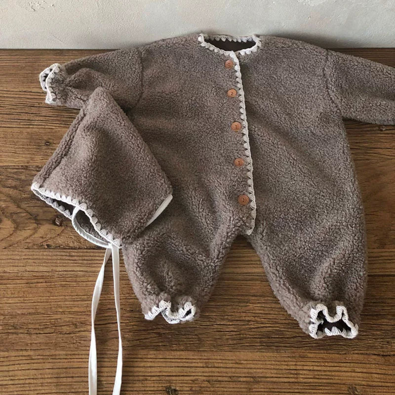 Mocha plush baby romper with tie bonnet laid on a wooden table