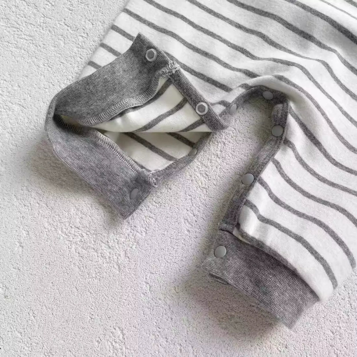 Snap fastenings along the legs of a grey striped baby onesie