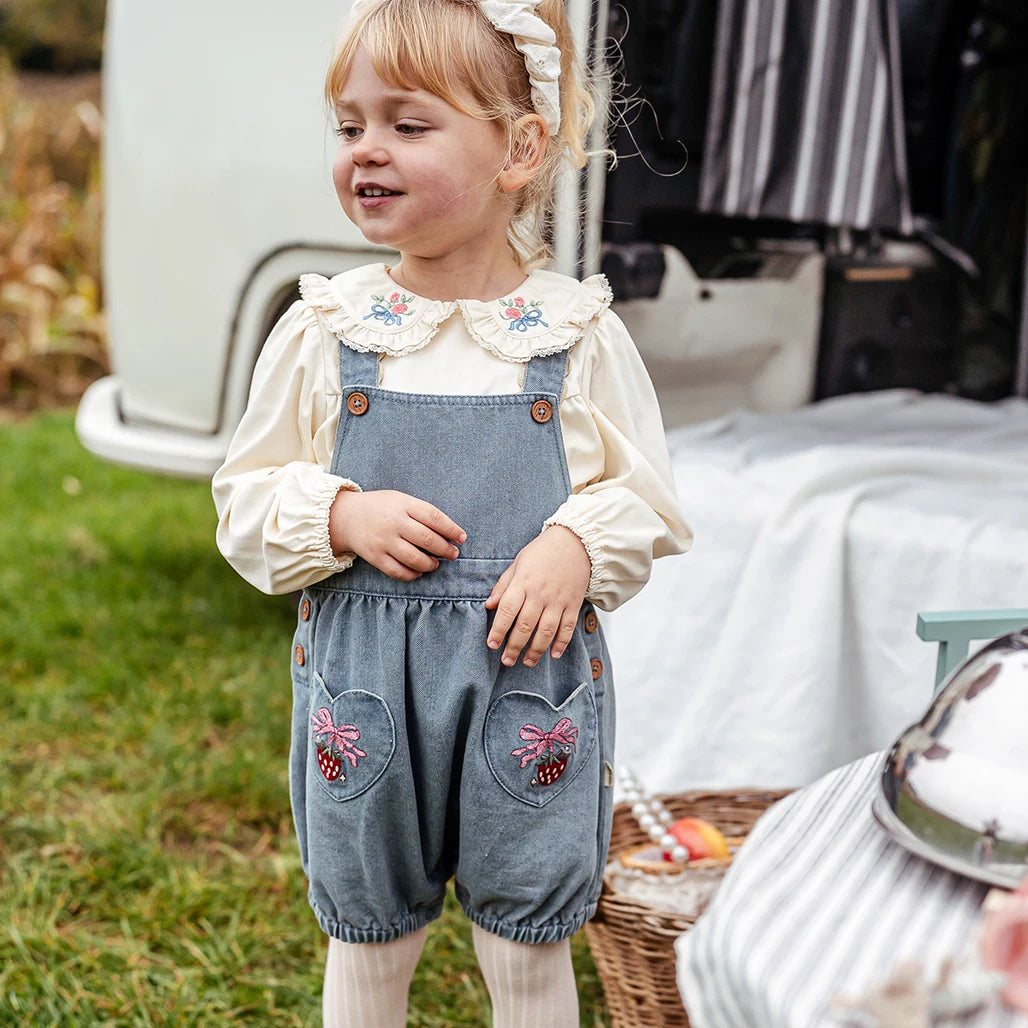 Little girl in denim blue strawberry shortalls and a frilled-collar blouse