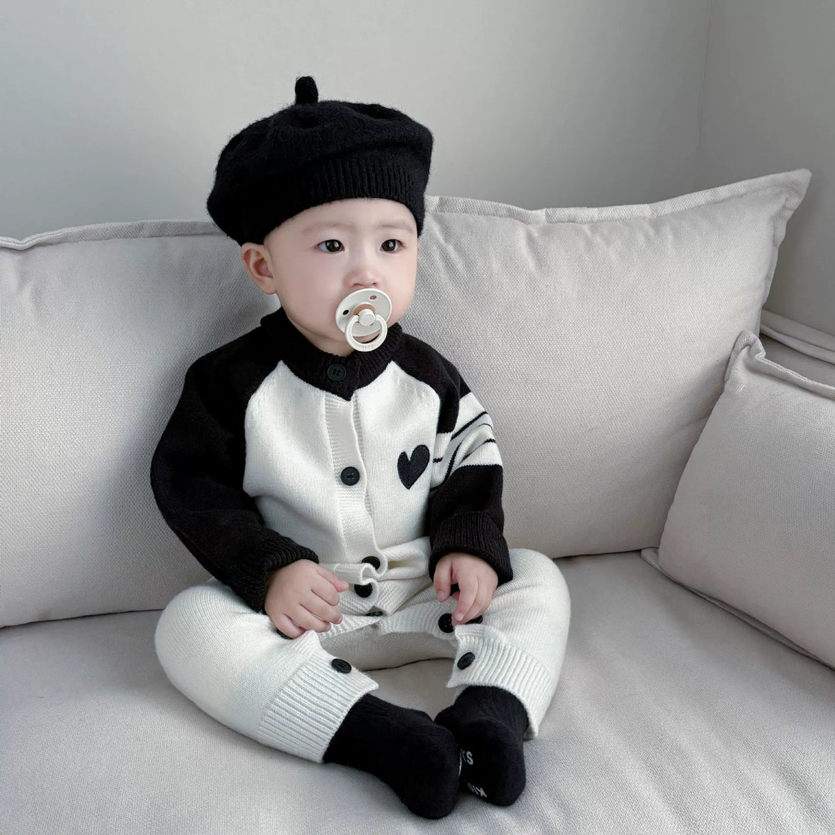 Baby sitting on a sofa in the heart knit sweater romper