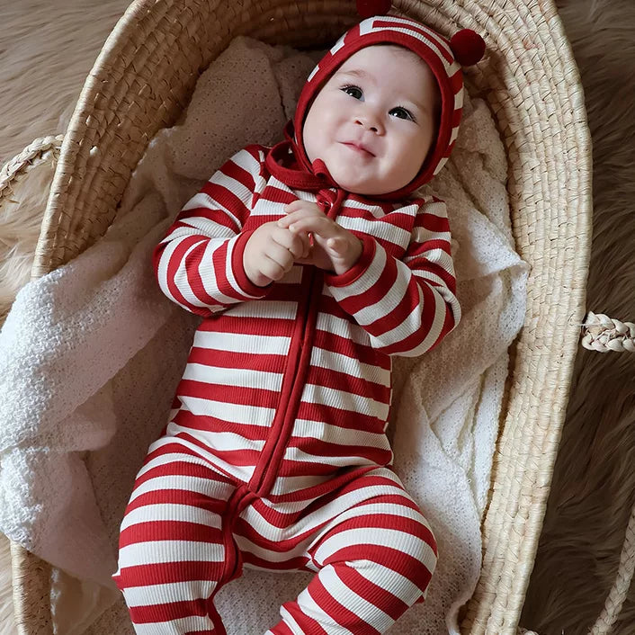 Baby lying in a moses basket in a red striped zip romper