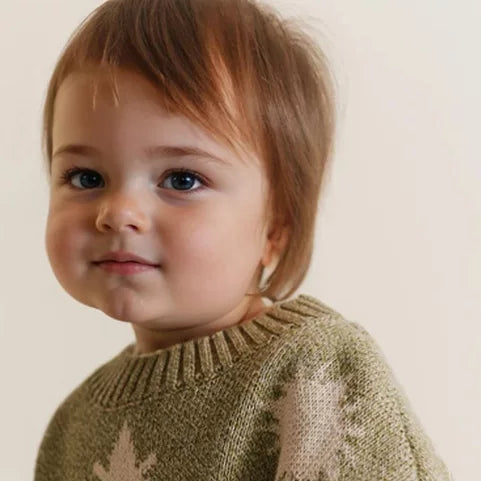 Toddler in an oversized olive sweater with sun and star motifs