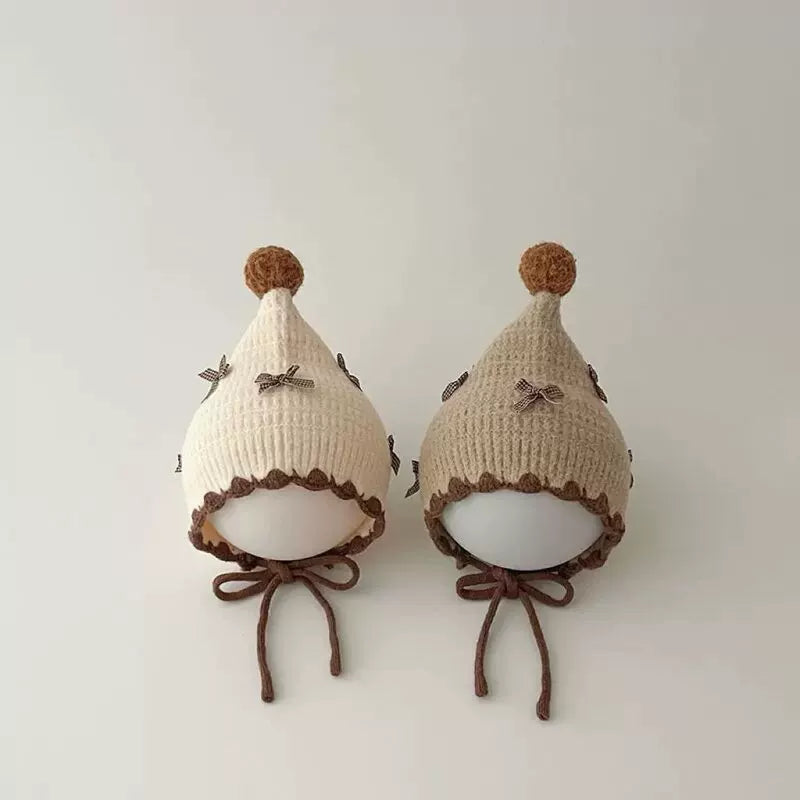 Cream and oat pixie bonnets with pom-poms on display heads