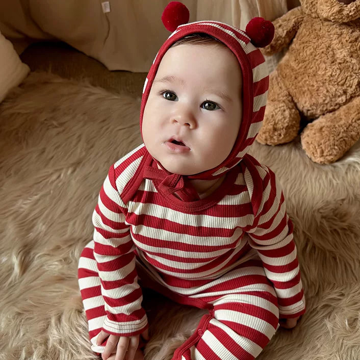 Baby sitting on a fluffy rug in a red and cream striped ribbed romper