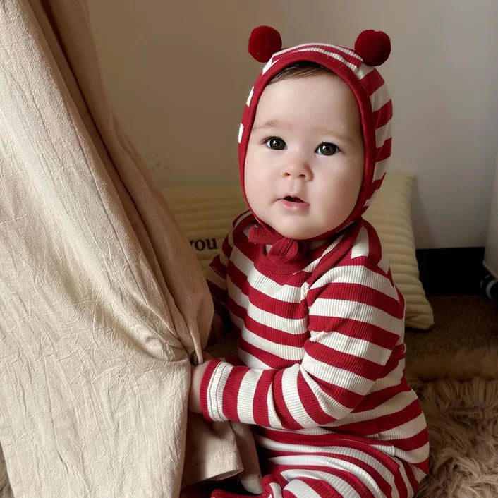 Baby sitting by a canvas tent in a red candy stripe romper