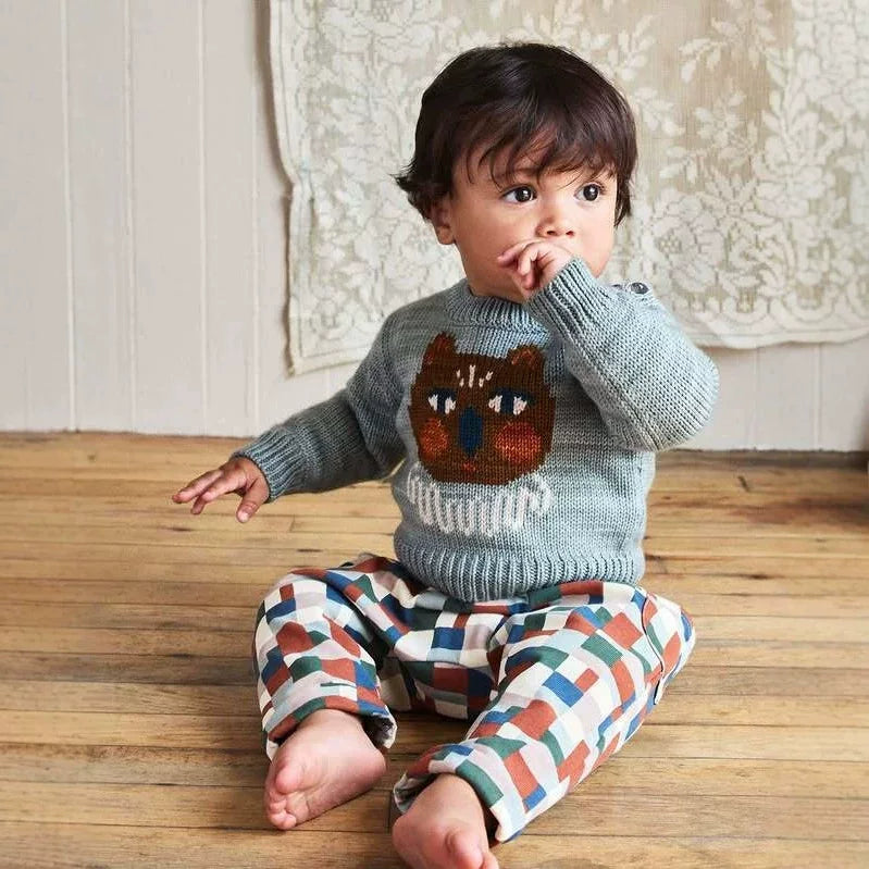 Toddler sitting on a wooden floor in a misty blue cat knit jumper