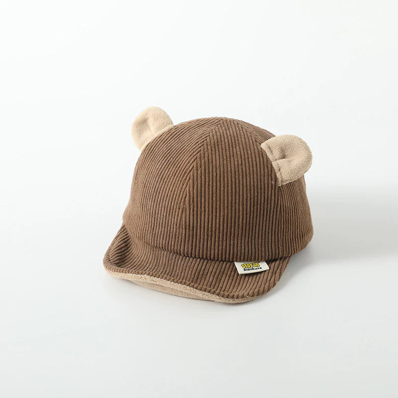 Children’s brown cap with a ribbed texture and adorable bear-like ears on top. The cap has a small label on the front and features a cozy, soft brim, adding a playful and charming touch to the design.