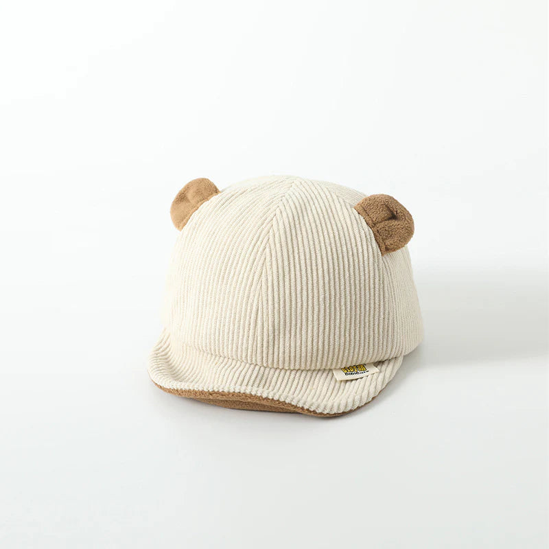 Children's cream-colored cap with a ribbed design and soft bear ears on top. The cap features a small branded label on the front brim, creating an adorable and cozy look perfect for young kids.