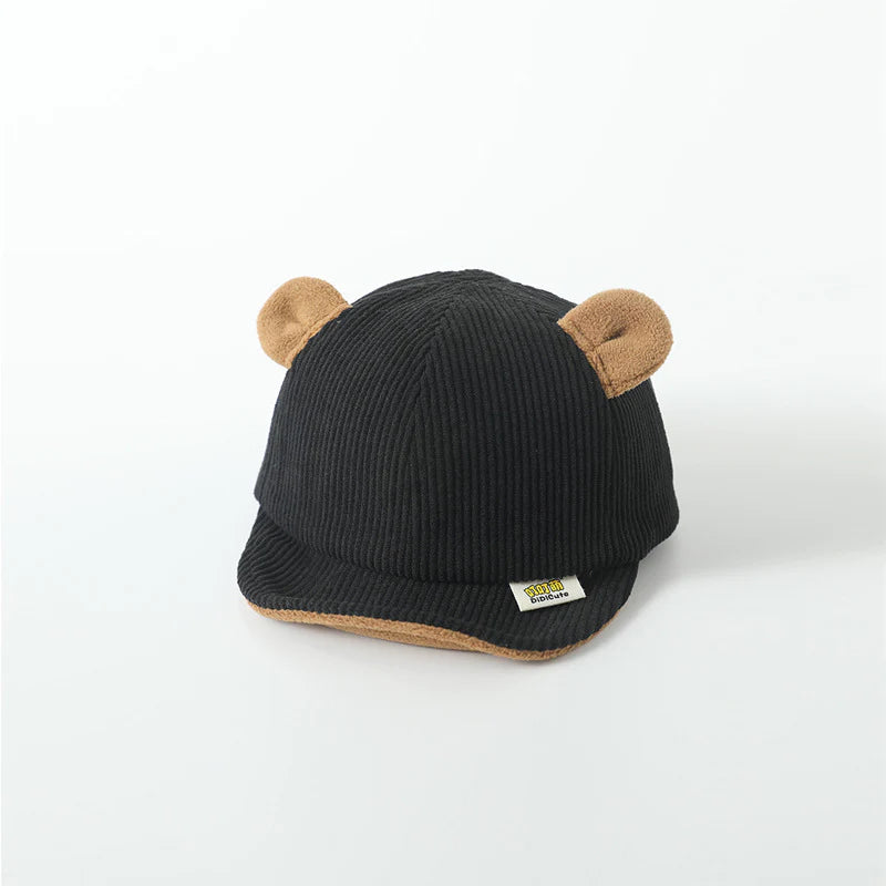 Children's black cap with a ribbed texture and soft brown bear ears on top, adding a playful and cozy design for young wearers. The cap features a small branded label on the front brim, complementing the cute and stylish look.