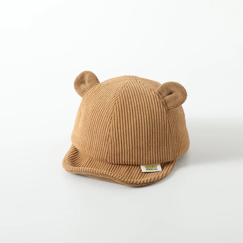 Children's brown cap with ribbed texture, featuring soft bear ears on top for a cute, playful look. A small branded label decorates the front brim, adding a stylish detail to this cozy accessory for kids