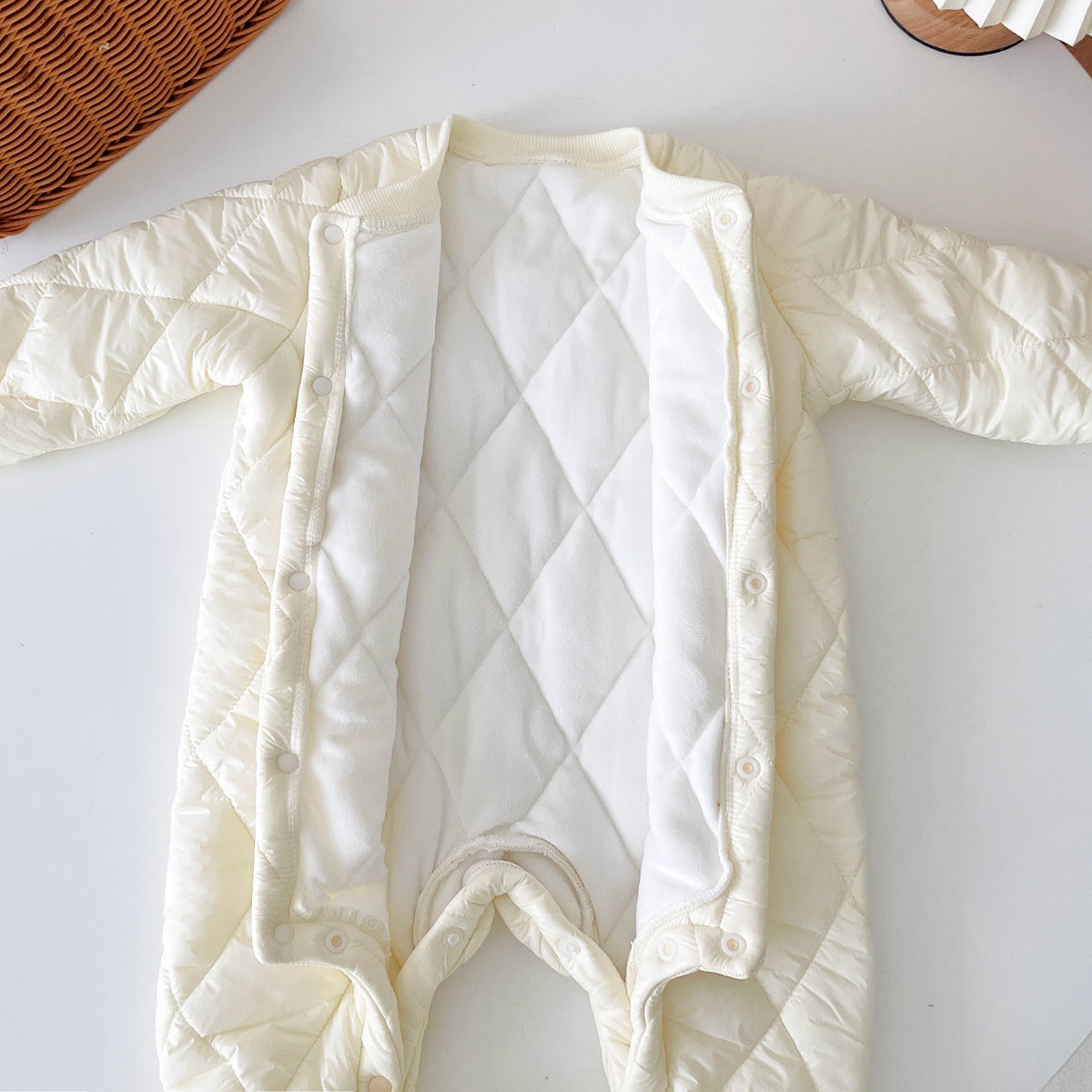 Open view of a cream-colored, quilted baby jumpsuit showcasing its soft, fleece-lined interior. The jumpsuit has a diamond quilt pattern on the outside, snap buttons along the front for easy closure, and extra padding for warmth, ideal for colder weather.