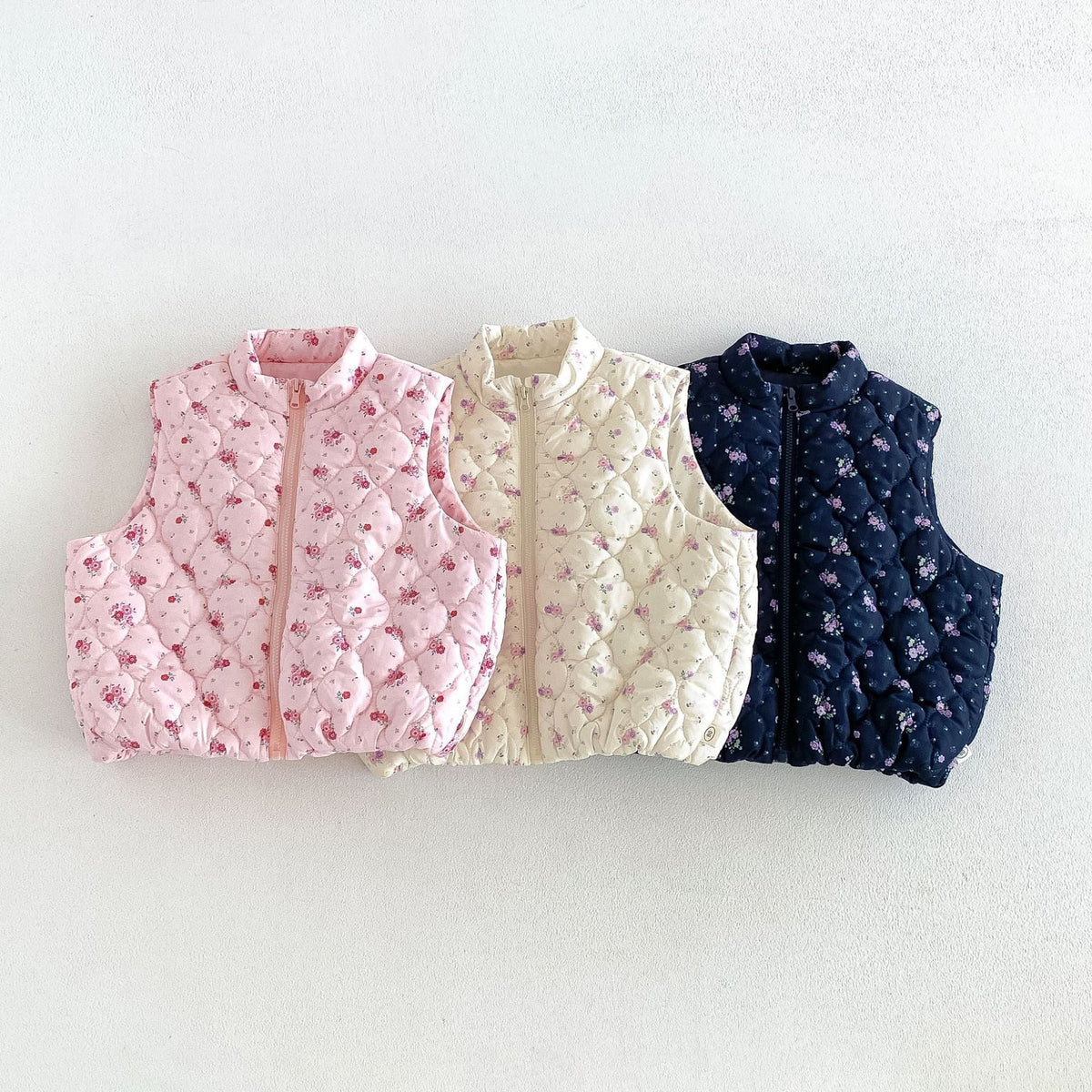 Cream, pink and navy floral quilted puffer vests laid side by side