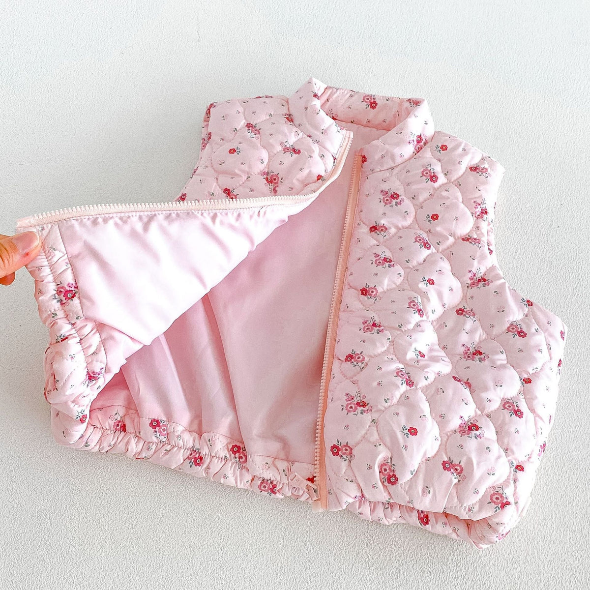 Open pink puffer vest showing the soft pink lining and gathered hem