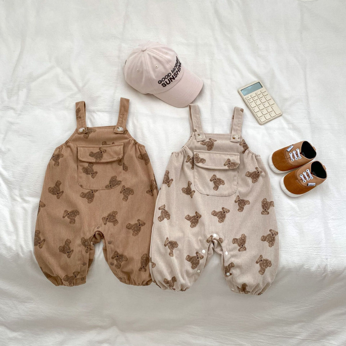 Brown and beige bear print baby dungarees flat lay with cap and shoes