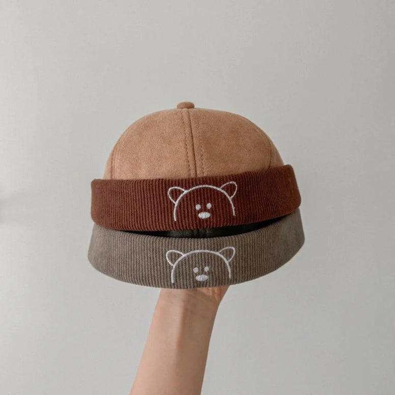 Beige and grey bear embroidered corduroy baby hats held in hand